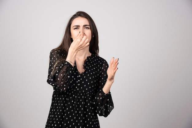 Una giovane donna che si copre il naso con la mano su un muro grigio.