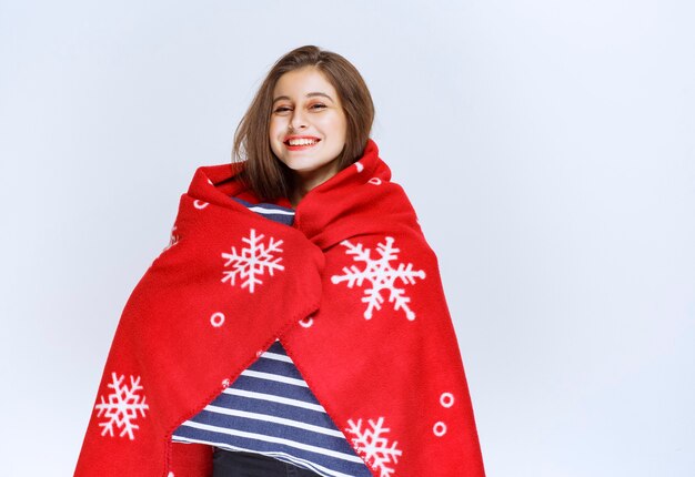 young woman covering herself with a red warm blanket and holding a blue striped blanket.