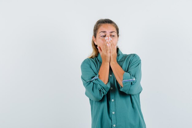 Young woman covering mouth and nose with hands in green blouse and looking annoyed