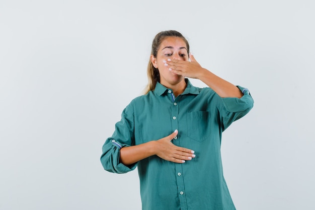 Young woman covering mouth with hand in green blouse and looking exhausted