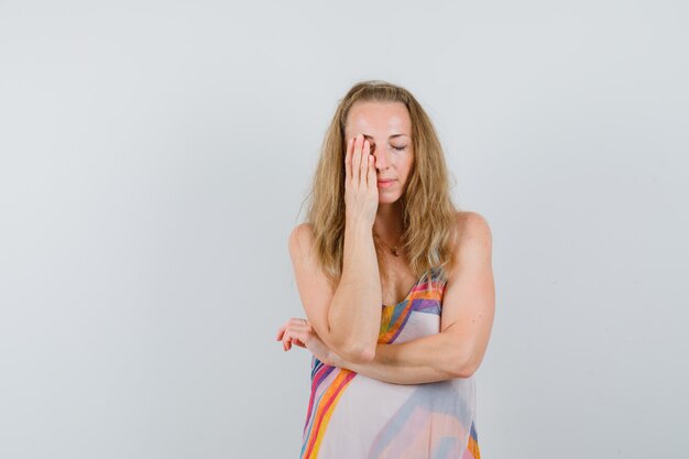 Young woman covering one eye with hand in summer dress and looking tranquil. 