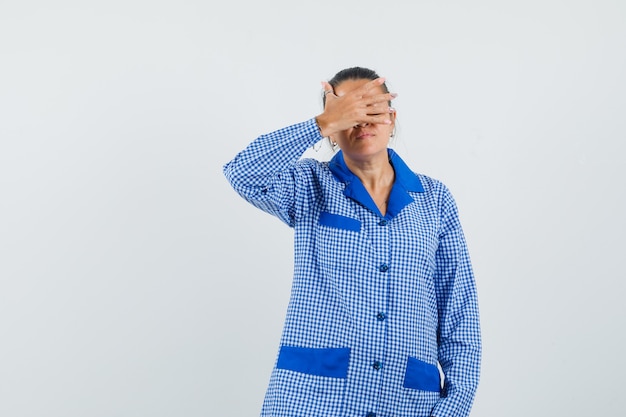 Young woman covering part of face with hand in blue gingham pajama shirt and looking serious , front view.