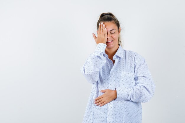 Young woman covering part of face with hand in white shirt and looking happy