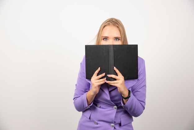 Young woman covering up her face with opened tablet on white.