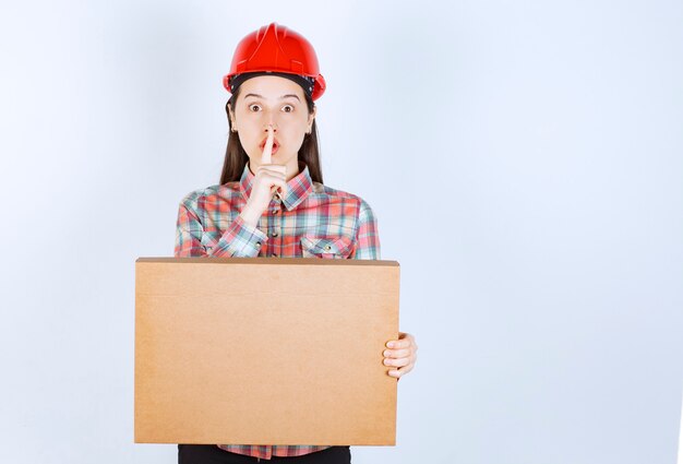 A young woman in crash helmet doing silent sign and holding paper box.