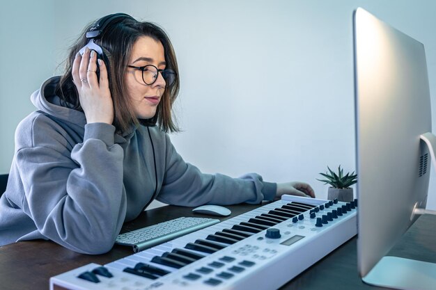 Free photo a young woman creates music using a musical keyboard and a computer