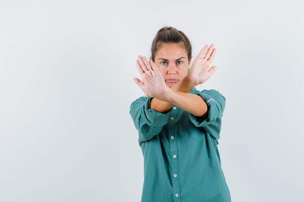 Молодая женщина, скрещивающая руки, показывает знак x или жест остановки в зеленой блузке и выглядит мило