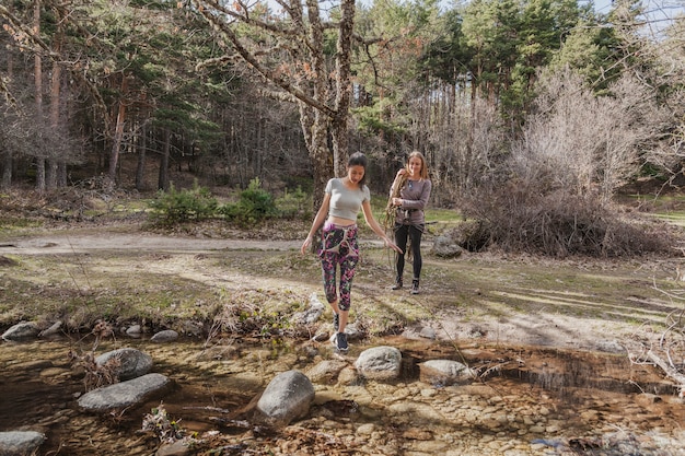 Young woman crossing a river with her friend