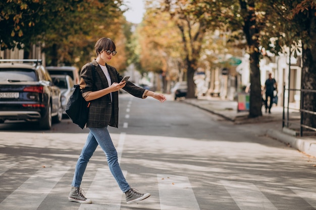 無料写真 道路を横断し、電話を使用して若い女性