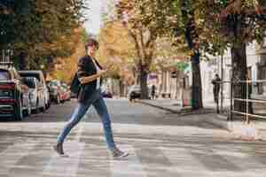 Free photo young woman crossing road and using phone