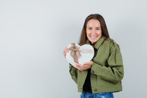 Young woman cuddling her gift in green jacket and looking merry. front view.