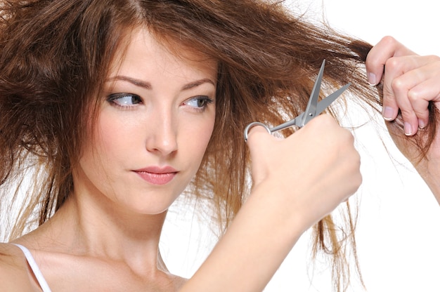 Free photo young woman cutting her backcombing brunette hair isolated on white