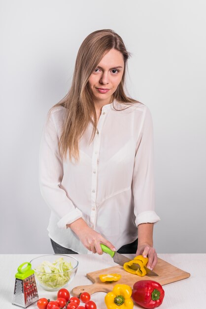 Young woman cutting yellow pepper on wooden board
