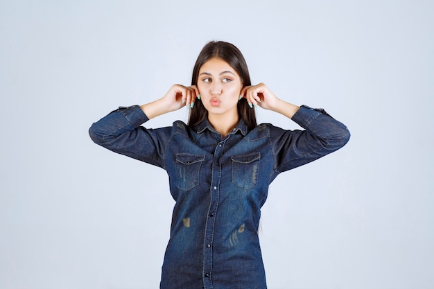 Young woman in denim shirt holding her ears