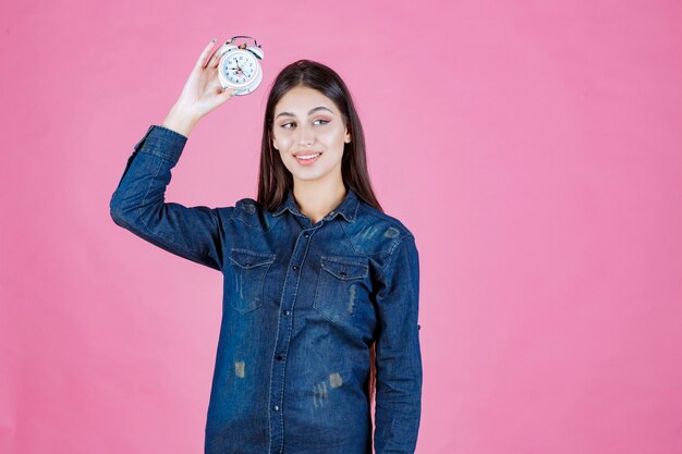 Young woman in denim shirt holding and promoting an alarm clock