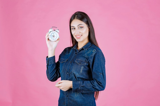 Young woman in denim shirt holding and promoting an alarm clock