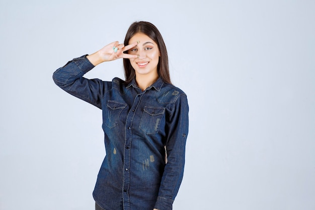 Young woman in denim shirt looking through her fingers