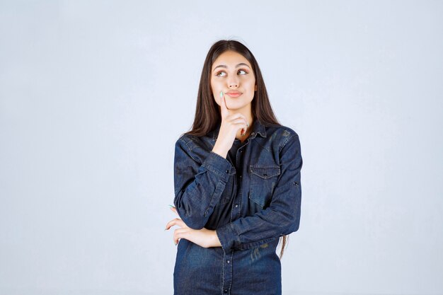 Young woman in denim shirt looks confused and thoughtful