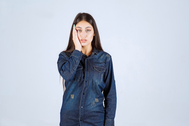 Young woman in denim shirt looks confused and thoughtful