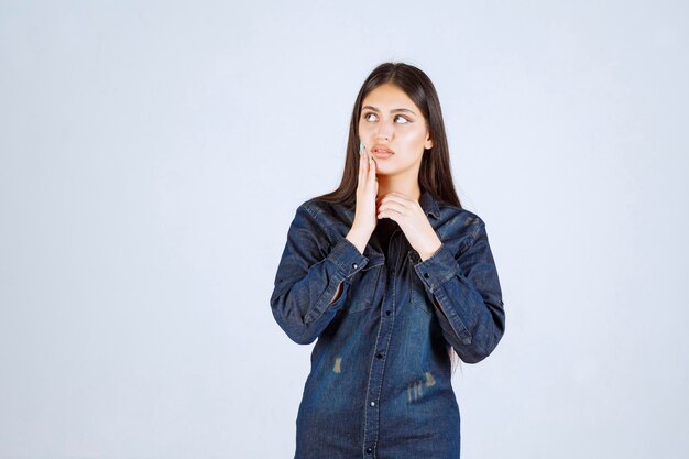 Young woman in denim shirt looks confused and thoughtful