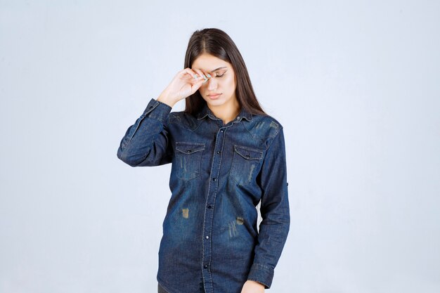 Young woman in denim shirt looks exhausted and sleepy