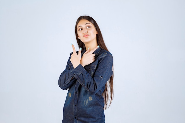 Young woman in denim shirt pointing at both sides