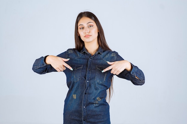 Young woman in denim shirt pointing downside