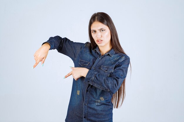 Free photo young woman in denim shirt pointing downside