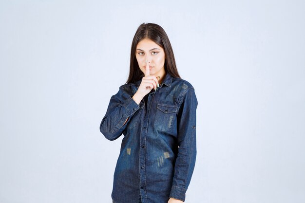 Молодая женщина в джинсовой рубашке, указывая на ее рот и прося молчать
