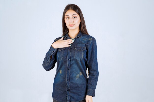 Young woman in denim shirt pointing at herself