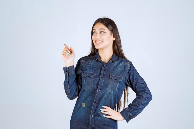 Молодая женщина в джинсовой рубашке, указывая влево с эмоциями лица