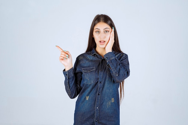 Young woman in a denim shirt pointing left side with face emotions