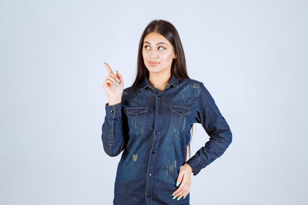 Young woman in a denim shirt pointing left side with face emotions