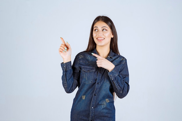 Young woman in a denim shirt pointing left side with face emotions