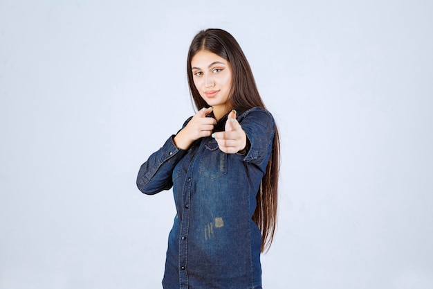 Young woman in denim shirt pointing at the person in front of her