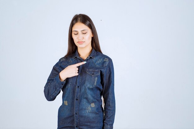 Young woman in denim shirt pointing at the right side