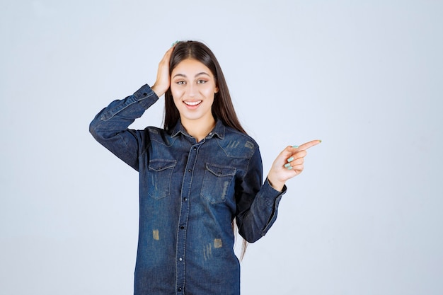 Young woman in denim shirt pointing at the right side