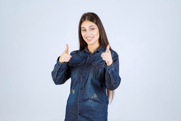 Young woman in denim shirt pointing someone ahead and inviting him