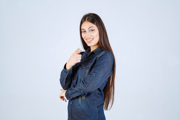 Young woman in denim shirt pointing someone ahead and inviting him
