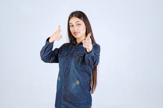 Young woman in denim shirt pointing someone ahead and inviting him