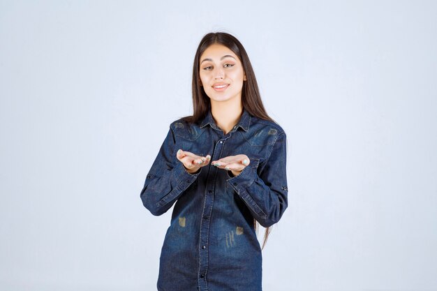 Young woman in denim shirt pointing someone ahead and inviting him