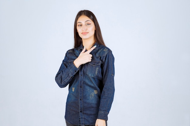 Young woman in denim shirt pointing at something on the right