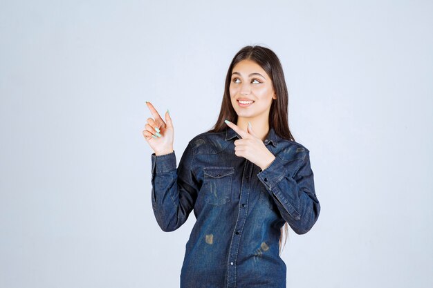 Young woman in denim shirt pointing at something in the upside