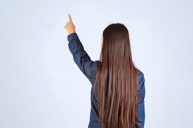Young woman in denim shirt pointing at something behind