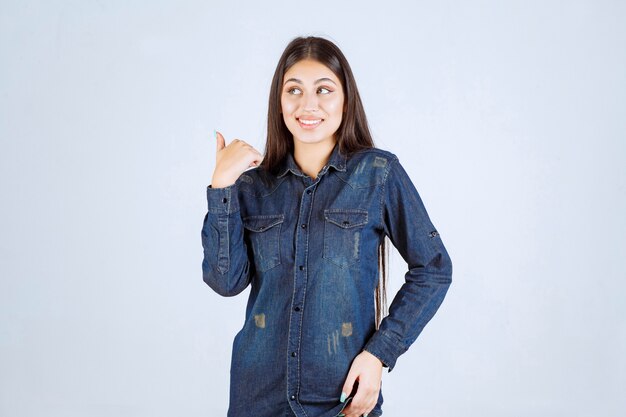 Young woman in denim shirt pointing at something behind