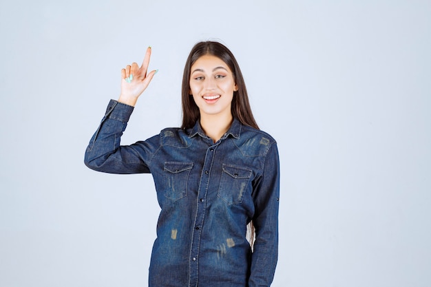 Young woman in denim shirt raising her hands up and pointing at something above