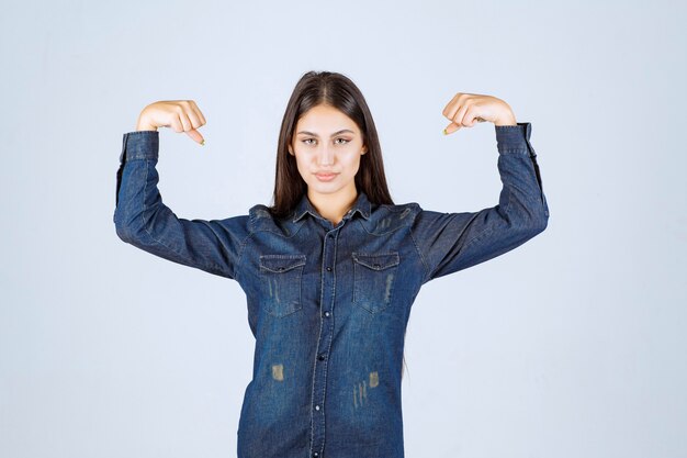 Free photo young woman in denim shirt showing her arm muscles