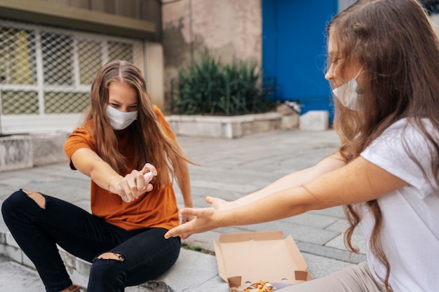 Молодая женщина дезинфицирует руки подруги перед едой пиццы