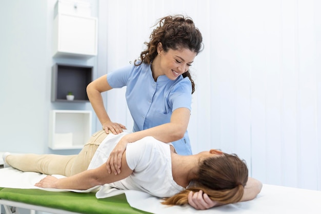 젊은 여성 의사 척추 지압사 또는 정골 의사는 수동 치료 클리닉을 방문하는 동안 누워 있는 여성을 손의 움직임으로 고정합니다. 작업 중 전문 척추 지압사
