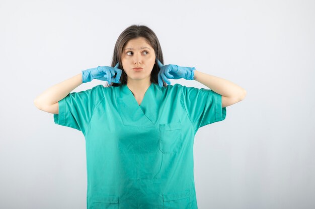 Young woman doctor in green uniform coning ears with index fingers.